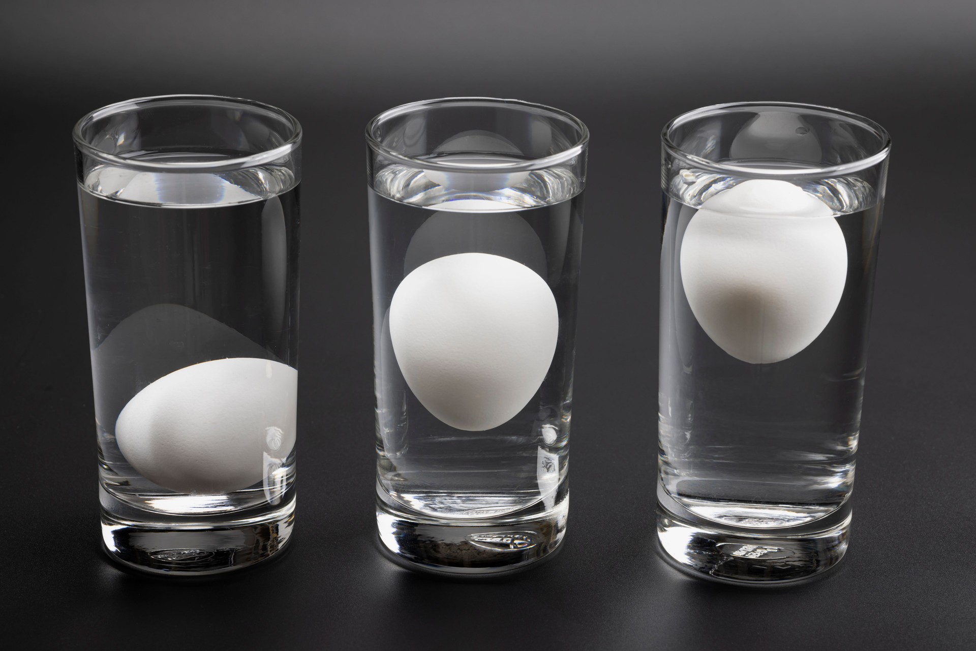 Eggs in water test on transparent glass , Egg freshness test on black background , Bad egg floats in water